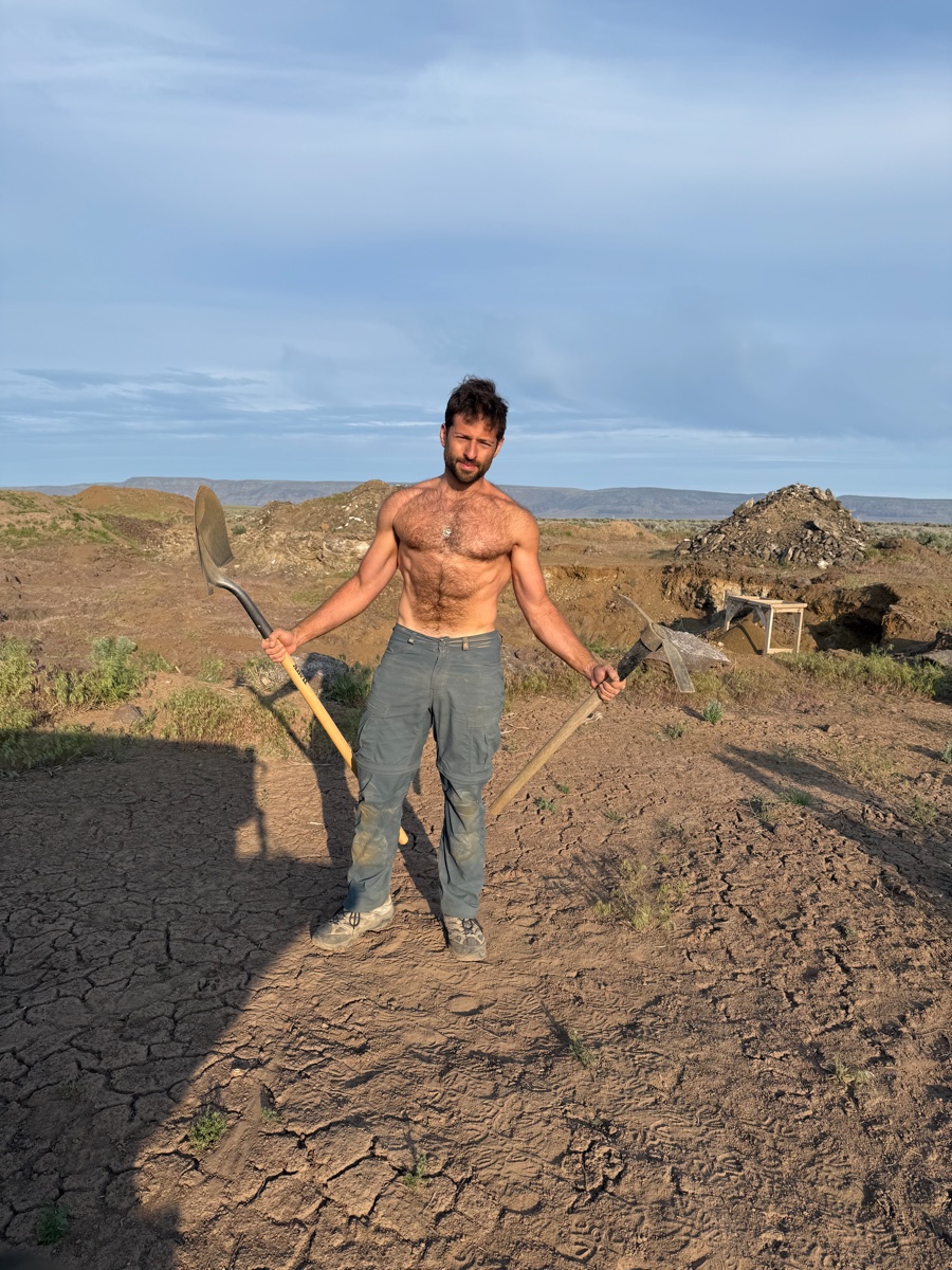 Zachary holding a shovel and pickaxe at a dig site