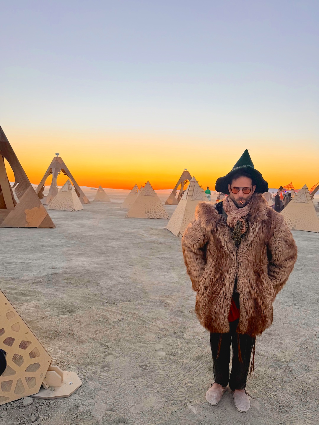 Zachary in a wide-brimmed hat among wooden sculptures at sunset