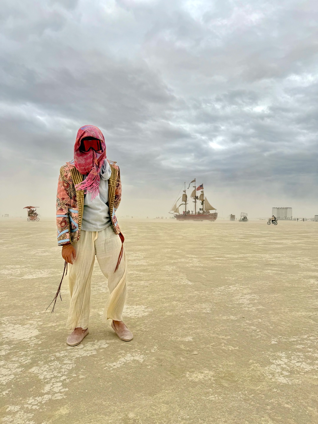 Zachary in a patterned jacket with a sailing ship on the dusty playa behind him